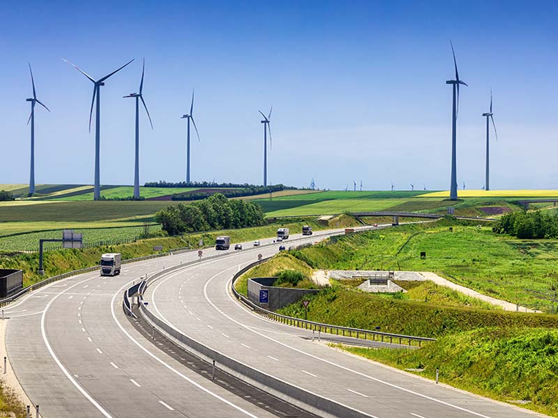 Autobahn entlang der Felder mit Windkraftanlage am Horizont