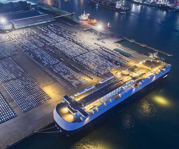 Luftaufnahme eines großen Frachtschiffs, das Autos und LKWs am Kai in den und aus dem Weltmarkt transportiert.