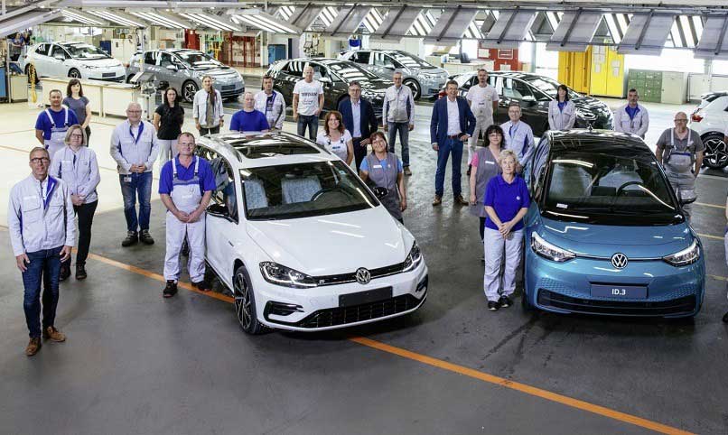 VW Werk mit Mitarbeitern die um einen VW ID.3 und Golf stehen