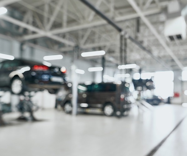 Reparatur-Service-Station mit angehobenen modernen Autos, die gewartet werden auf unscharfen Hintergrund mit vielen Diodenlampen.