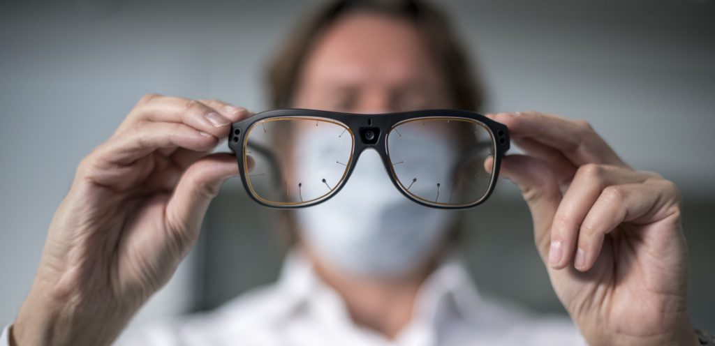 Brille mit Messdrähten, die ein Mann mit Maske im Hintergrund hält